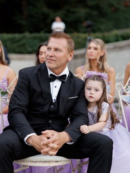 David Newman seated in a tuxedo beside his young daughter at an outdoor evening celebration