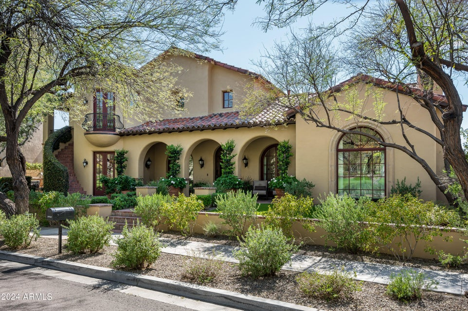 Street-level daytime view of 19946 N 103rd Street in North Scottsdale, a Spanish Colonial estate with a red clay tile roof, arched entryways and a Juliette balcony under a clear blue sky