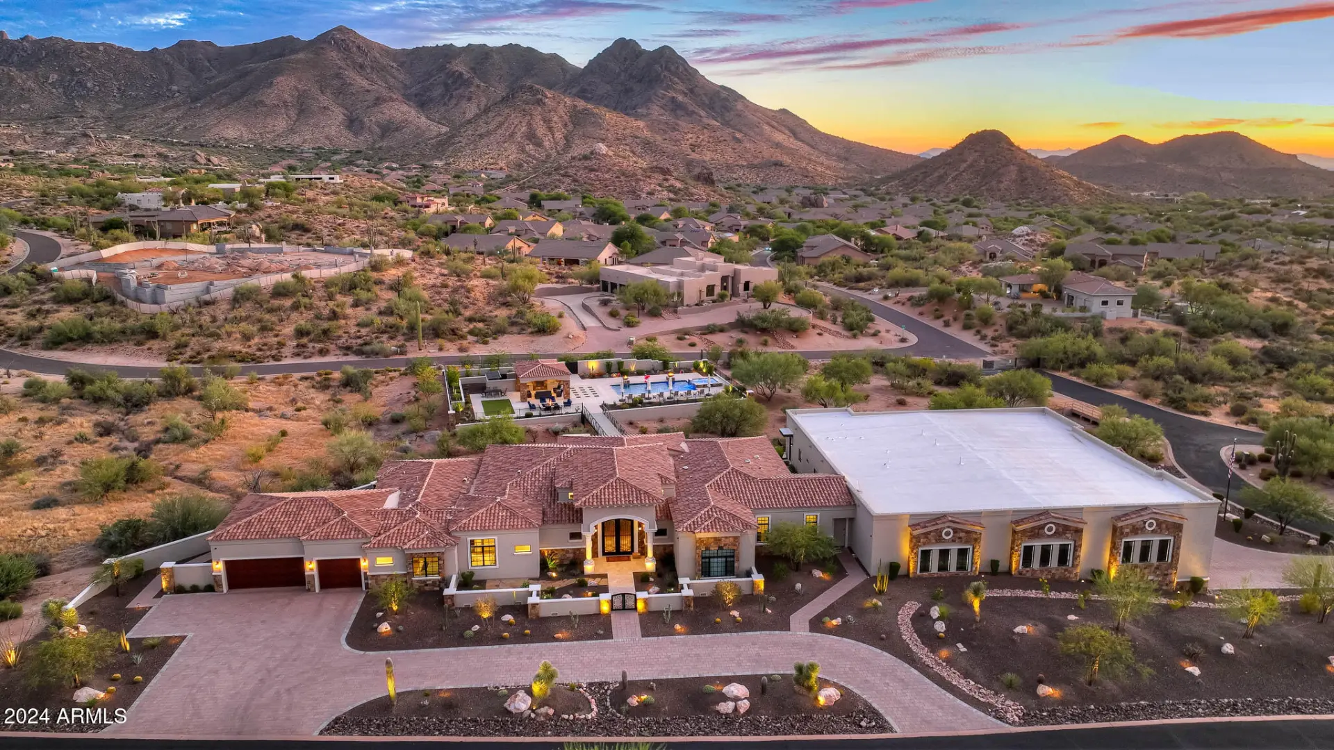 Aerial view at sunset of 11935 E Buckskin Trail in North Scottsdale with the McDowell Mountains behind and a lit pool and patio