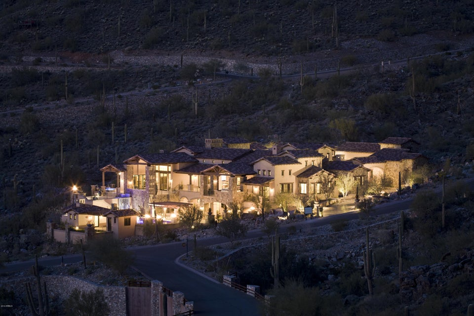 Aerial view at dusk of 11386 E Whistling Wind Way in North Scottsdale, a Mediterranean-style estate with clay tile roofs, stone and stucco walls and a lit pool among saguaro cactus