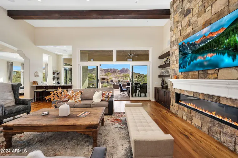 Great room at 11935 E Buckskin Trail with stone fireplace wall, wood beams and sliding glass doors
