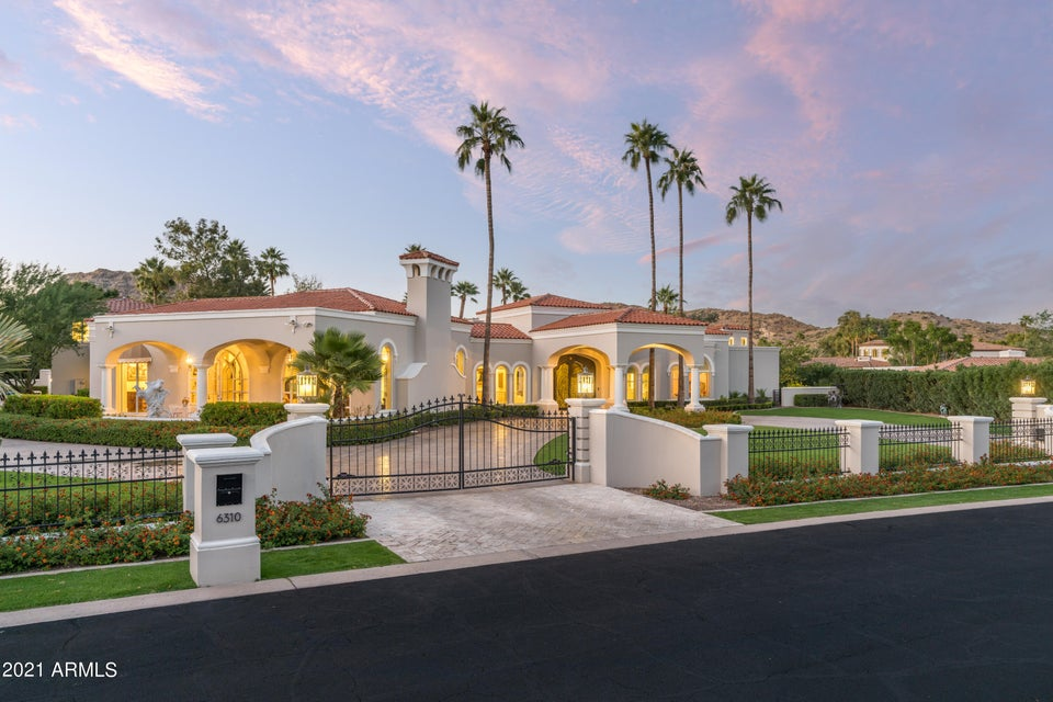 Front view at dusk of 6310 N Yucca Rd in Paradise Valley, a Mediterranean-style estate with arched loggias, clay tile roof and palm trees against a twilight sky