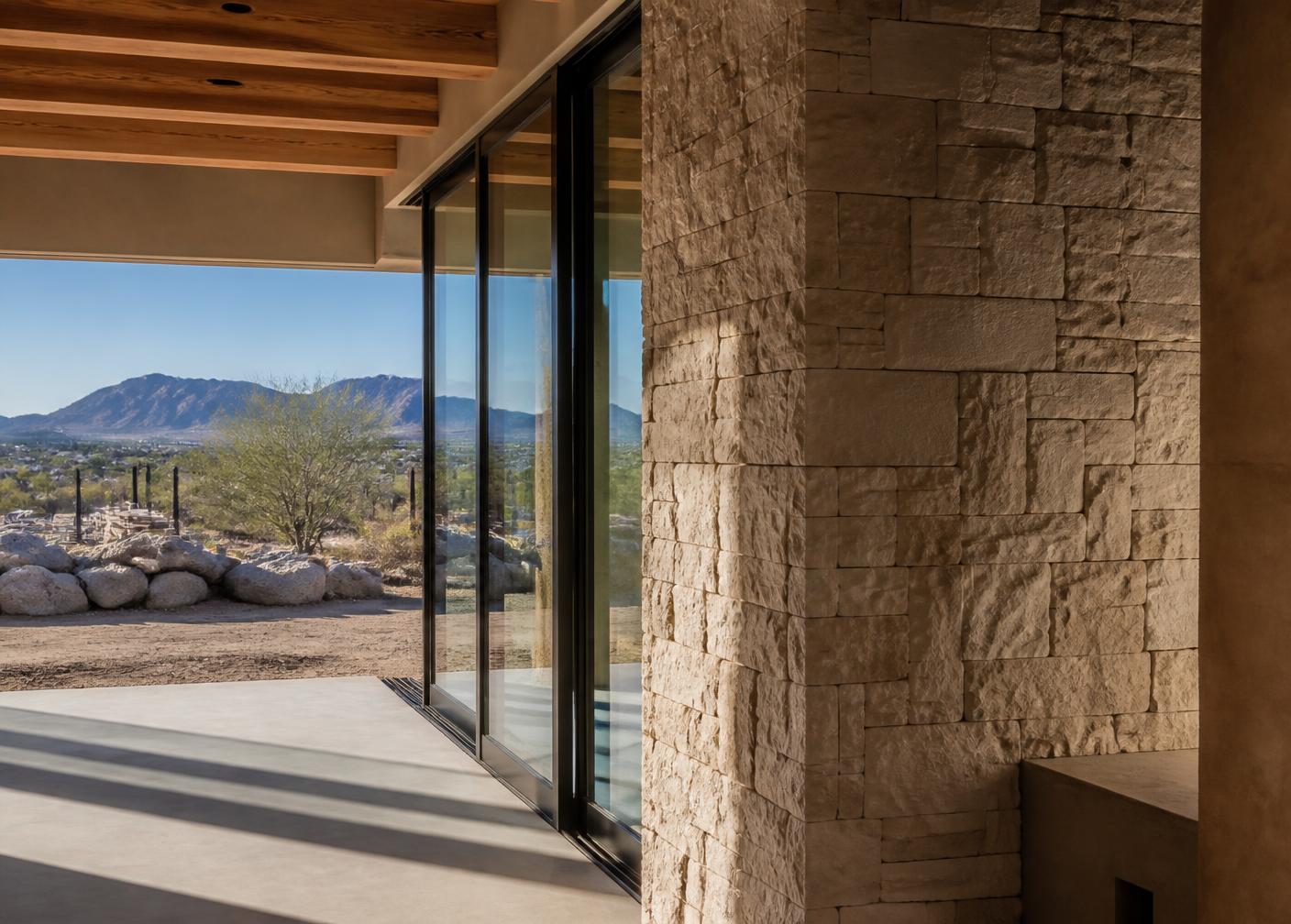 Limestone masonry wall meeting steel-framed glass and exposed wood ceiling beams in an Arizona desert home under construction