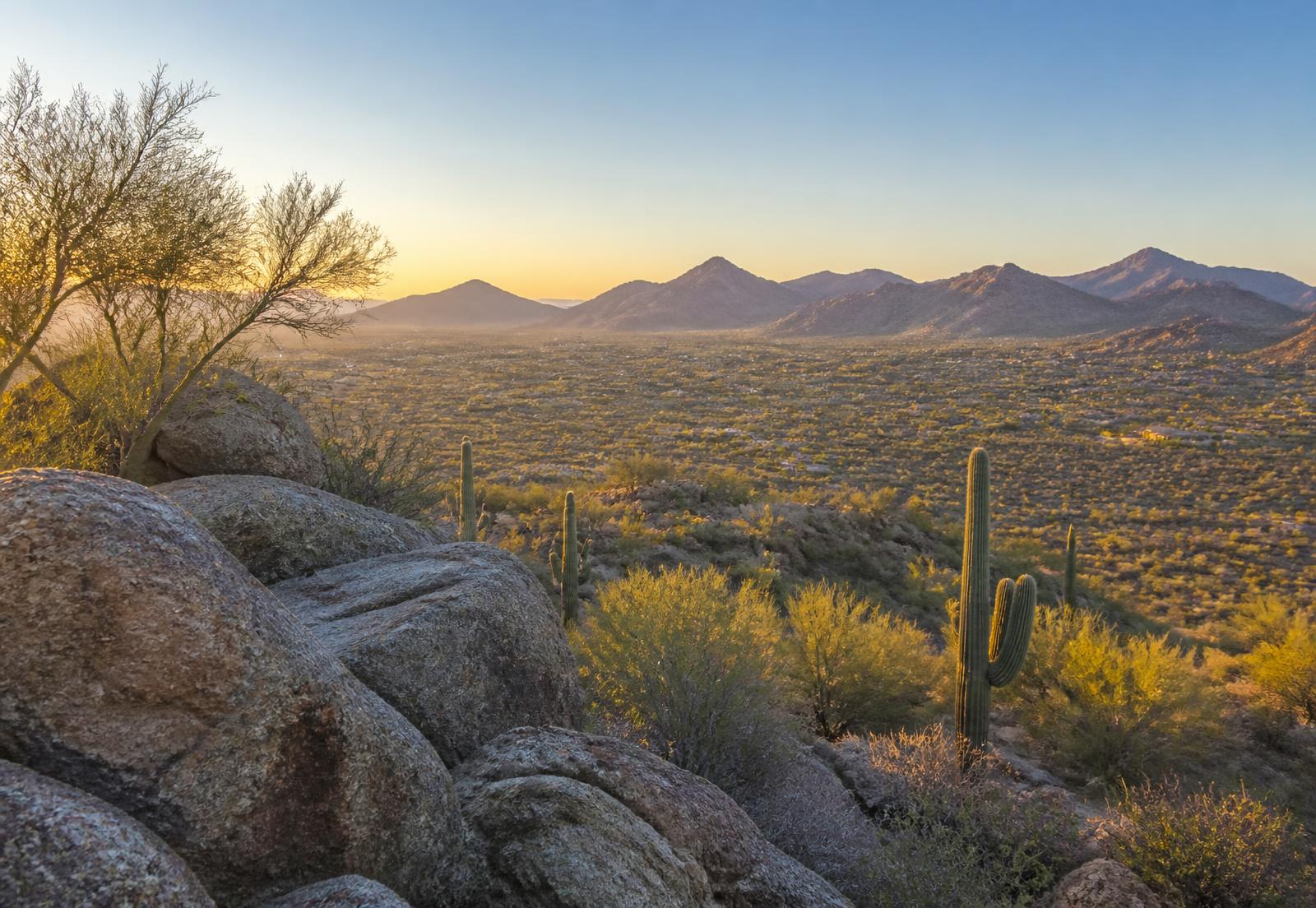 Elevated high-desert homesite in North Scottsdale at sunrise, with granite boulders, palo verde and saguaro overlooking a broad Sonoran Desert valley and layered mountain ranges