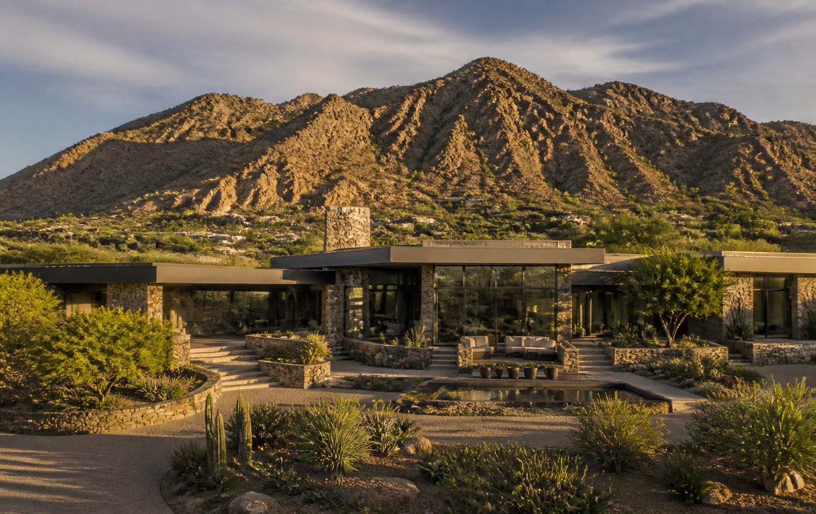 Distinctive custom Paradise Valley estate of stone and glass on a large private lot beneath a desert mountain in late afternoon light