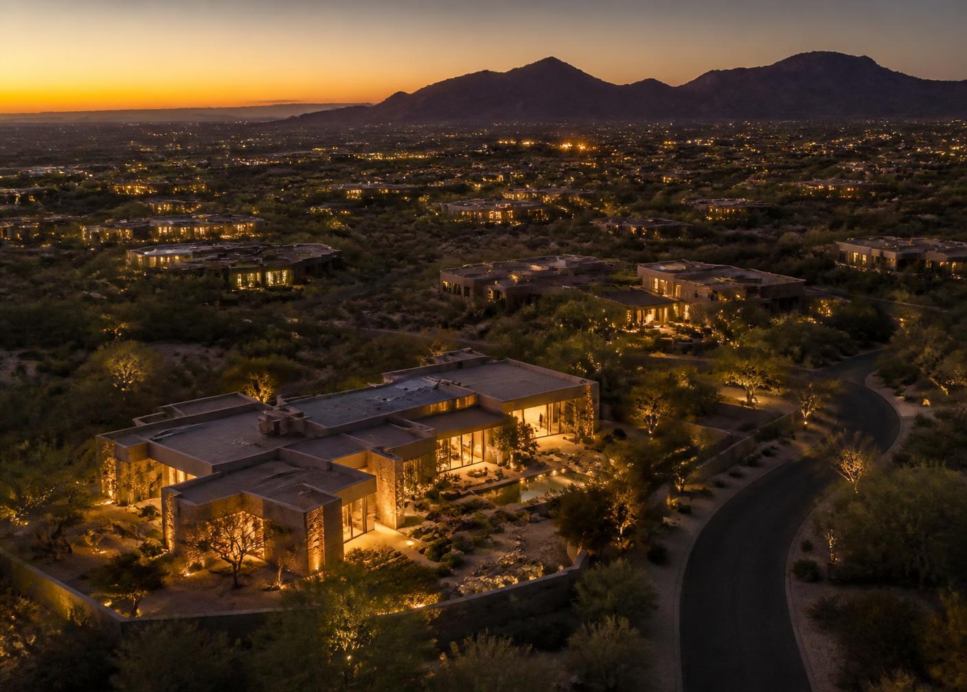 Aerial view at dusk of an exclusive Scottsdale luxury neighborhood with lit desert residences and a mountain ridgeline