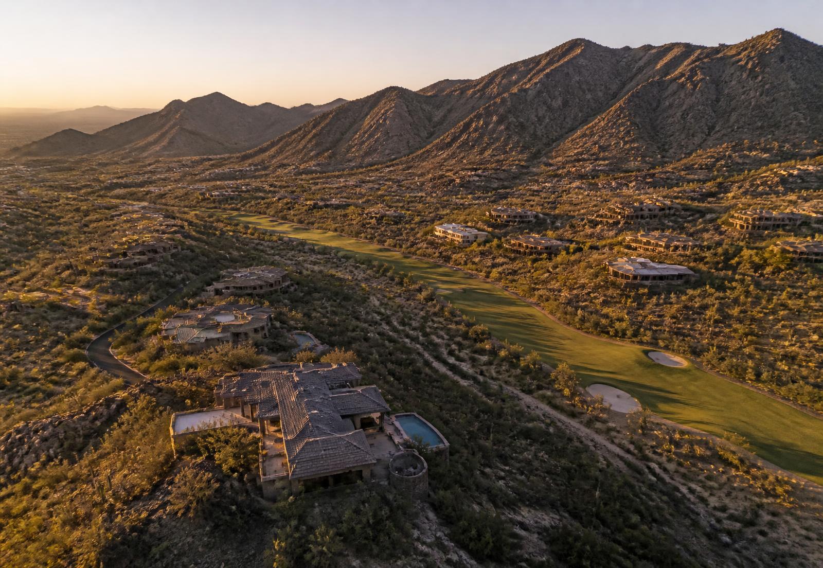 Golden hour aerial view of a North Scottsdale desert mountain luxury community with large custom estates on elevated lots and a private golf corridor winding between them