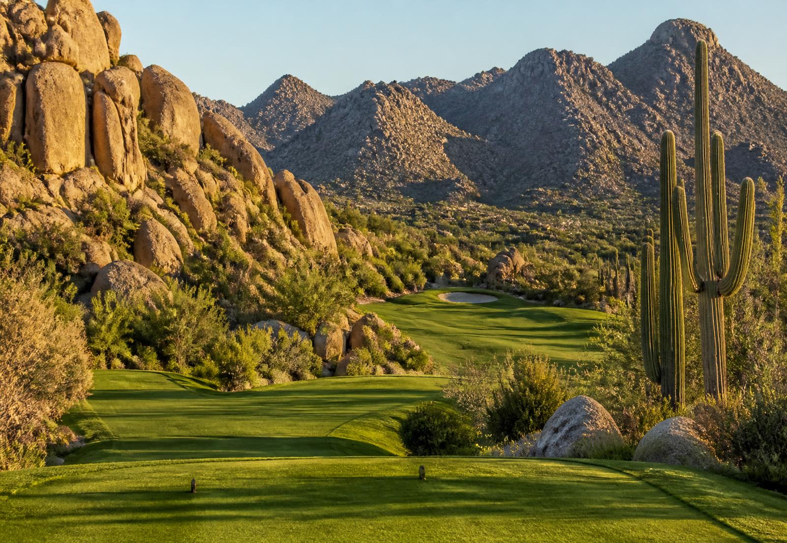 Desert golf fairway winding between granite boulder outcroppings and saguaro cactus in the high Sonoran Desert foothills of North Scottsdale in late afternoon light