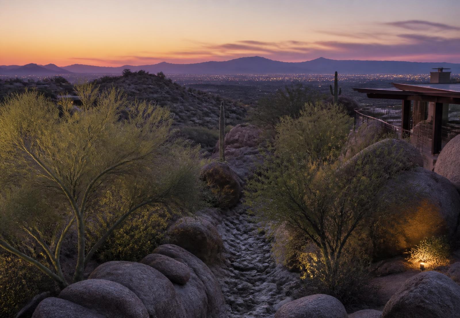 Elevated North Scottsdale hillside home site at dusk with granite boulders, palo verde trees and a natural desert wash overlooking layered mountain ridges and distant valley lights